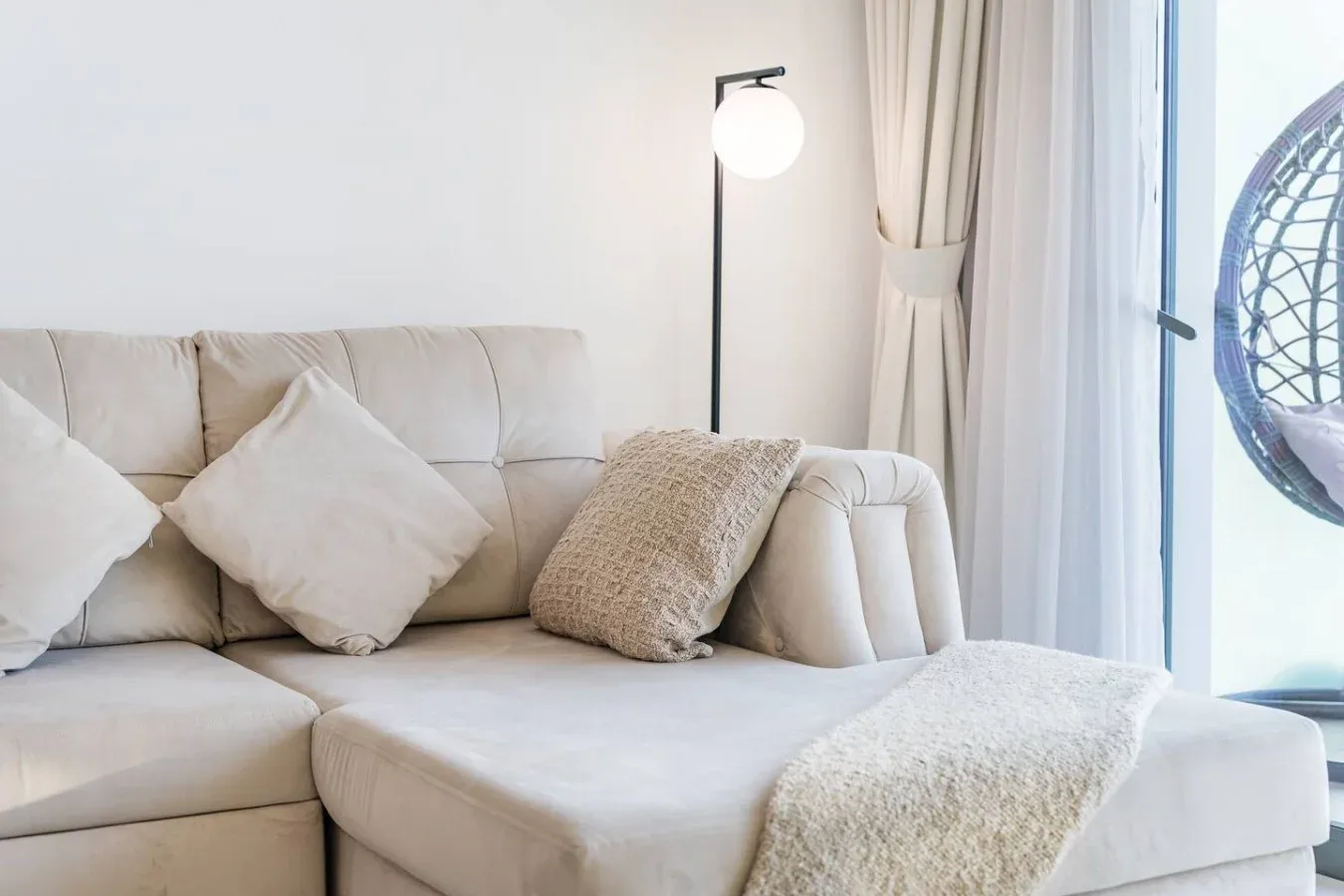 Una sala luminosa con sofá seccional claro, cojines y una lámpara de pie.