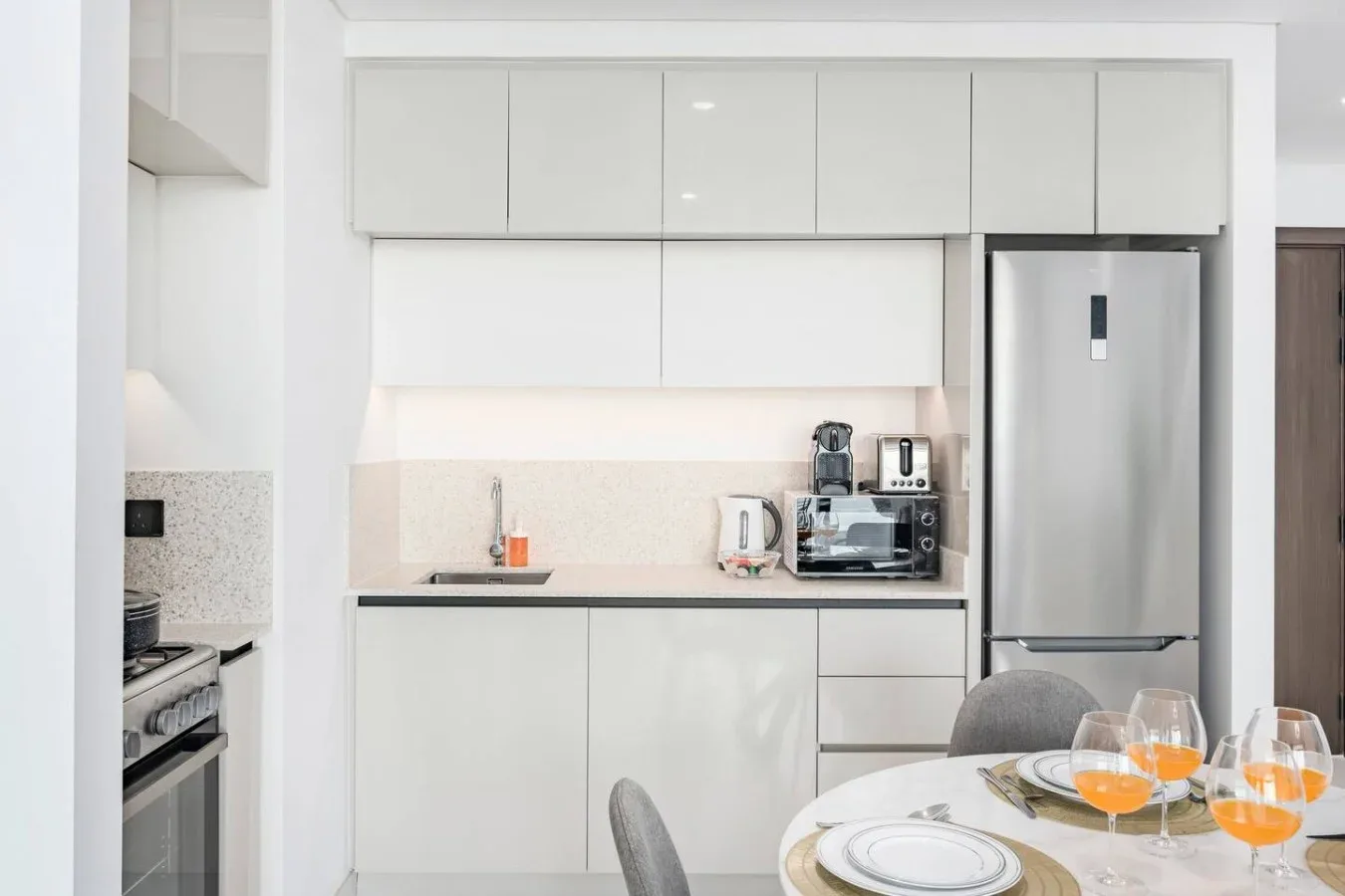 Una cocina moderna y luminosa con gabinetes blancos, electrodomésticos de acero inoxidable y una mesa de comedor.