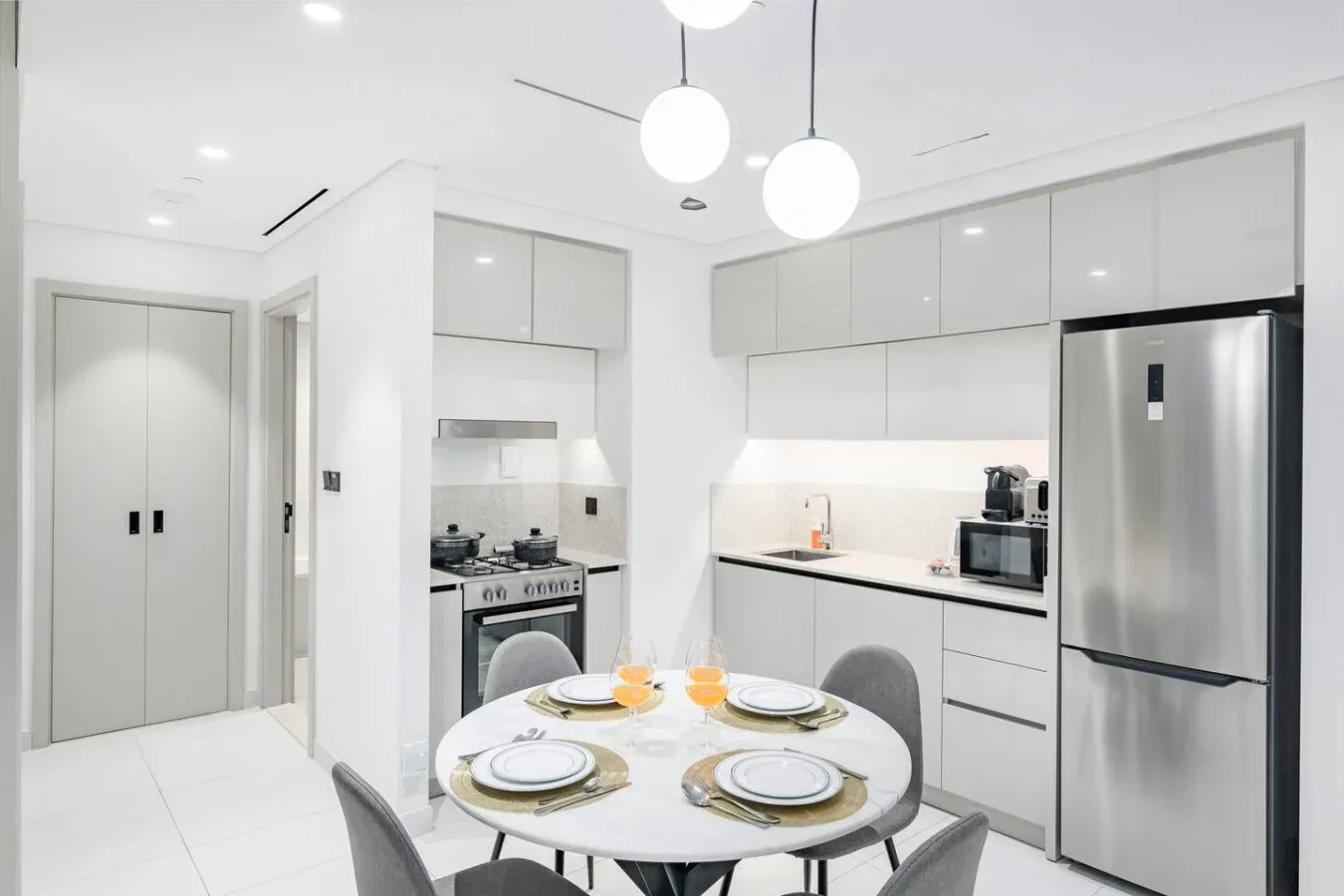 Una cocina blanca y luminosa con una mesa redonda y electrodomésticos de acero inoxidable.