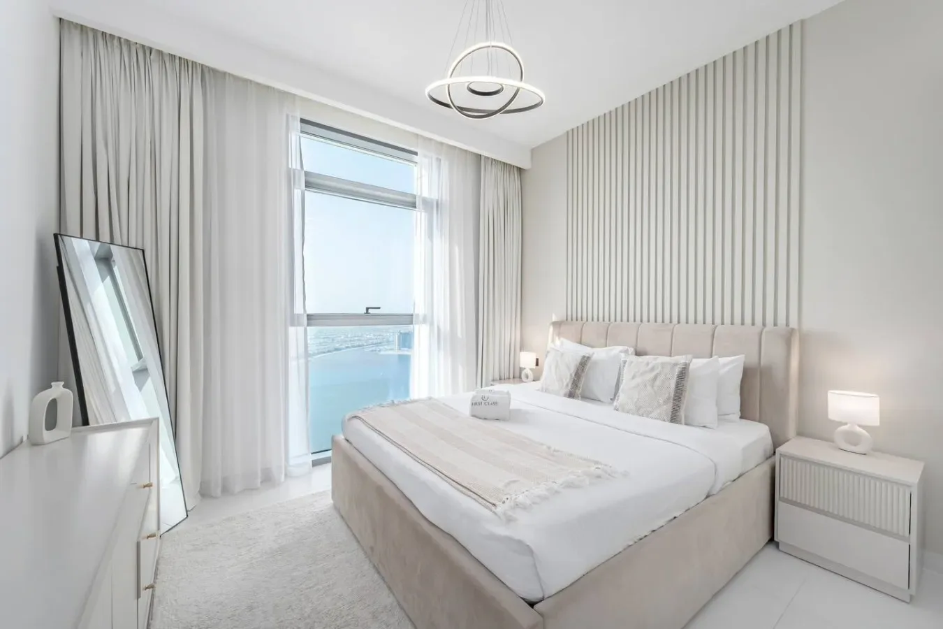 Un dormitorio luminoso con una cama bien hecha junto a una ventana alta.