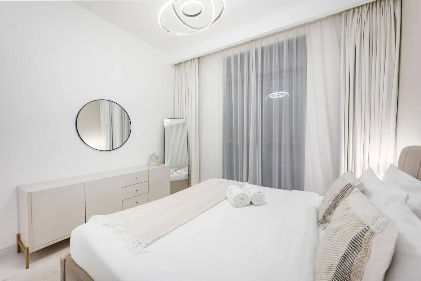 Un dormitorio luminoso con cama, cómoda y cortinas que cubren una ventana grande.