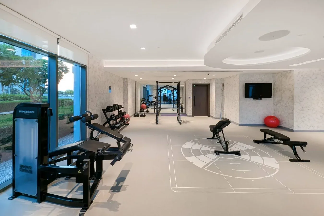Un gimnasio luminoso con equipos de ejercicio alrededor de una zona abierta para entrenar.