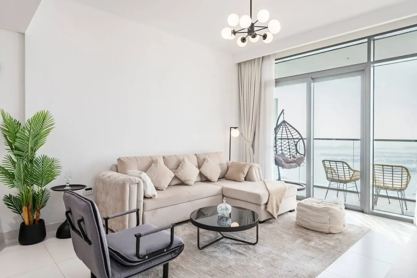Una sala de estar luminosa con un sofá seccional beige, una mesa de centro de vidrio y ventanales.