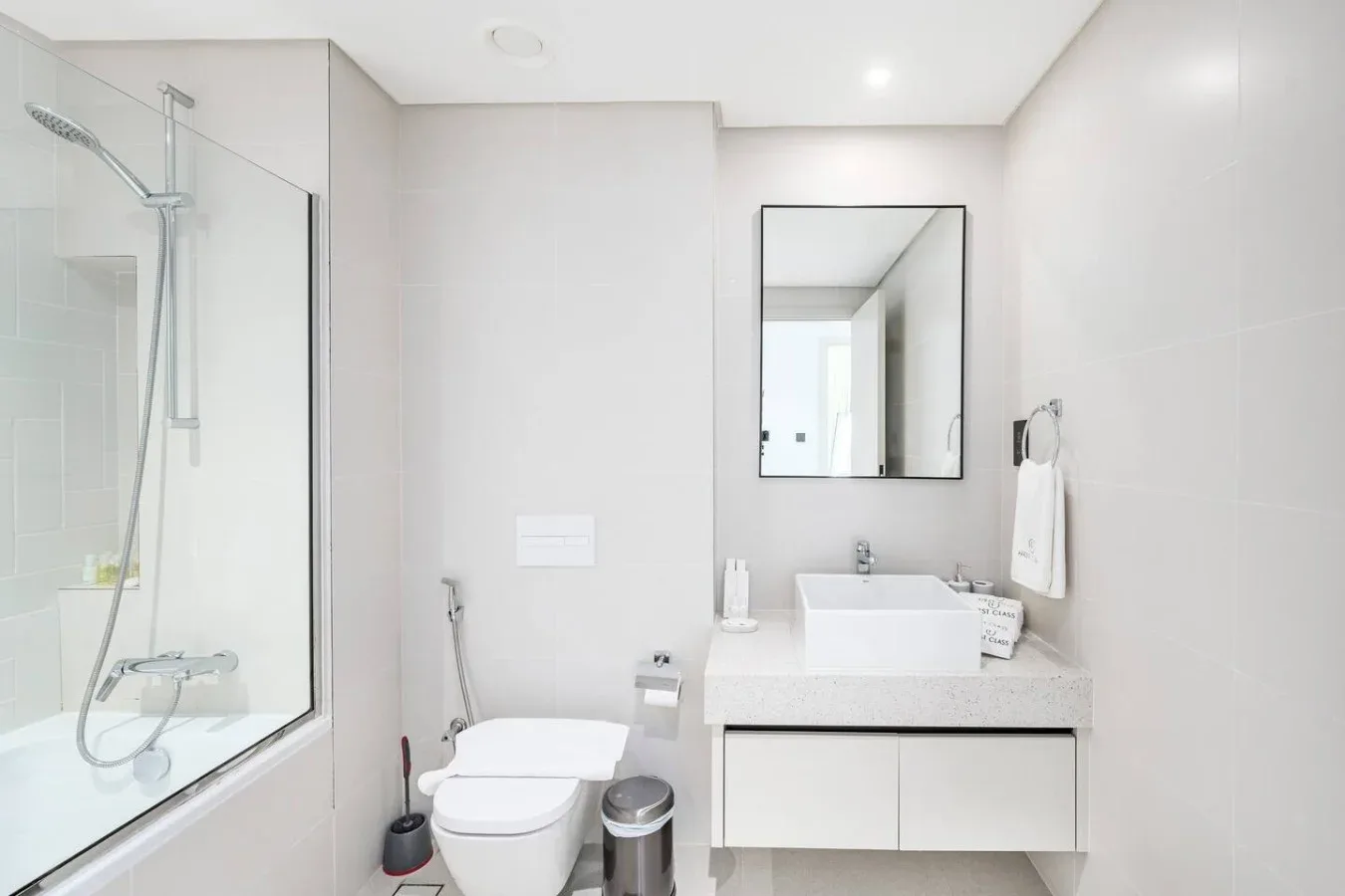 Un baño luminoso con ducha, inodoro y lavabo bajo un espejo de pared.