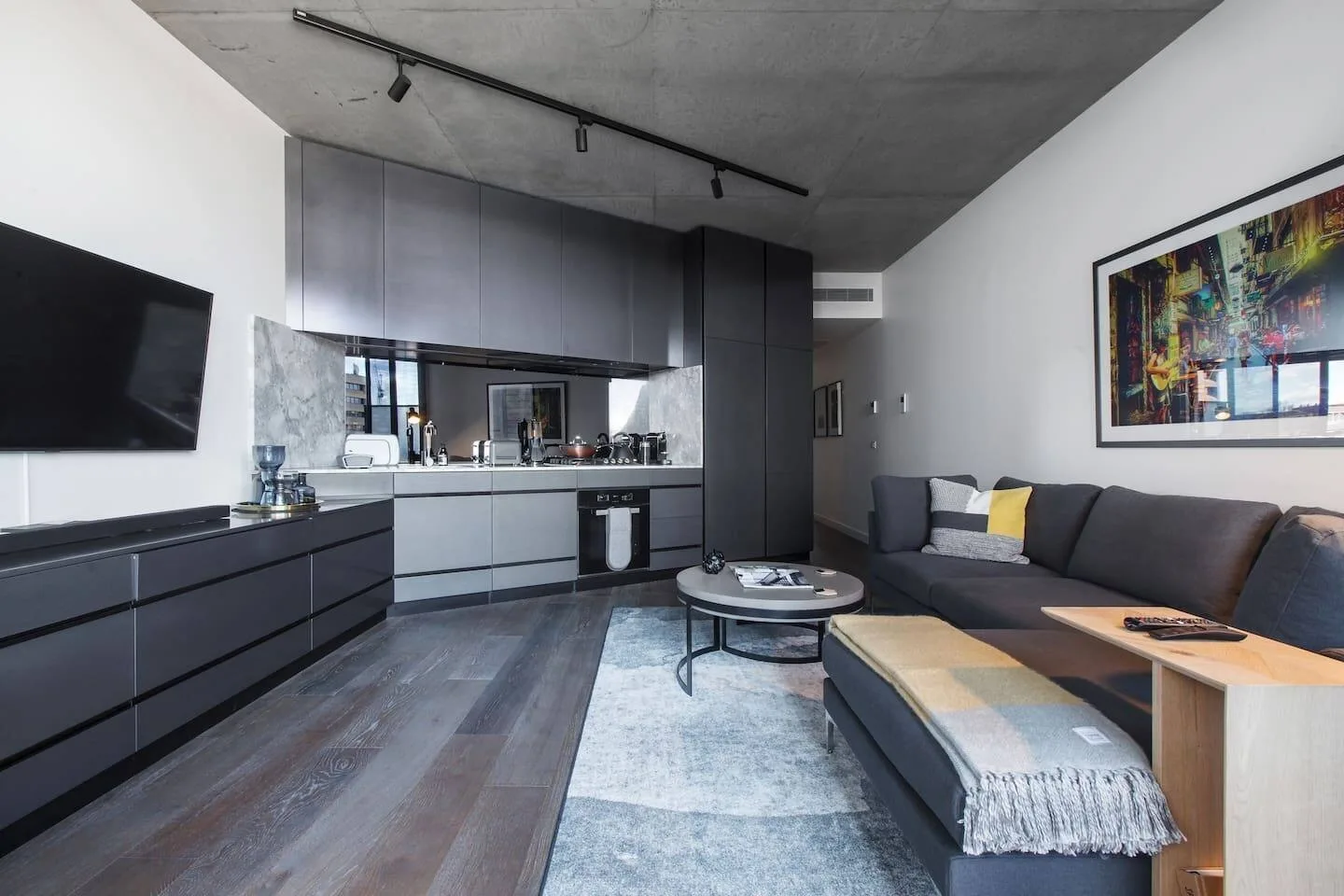 Una sala moderna con sofá seccional oscuro, mesa de centro y cocina abierta.