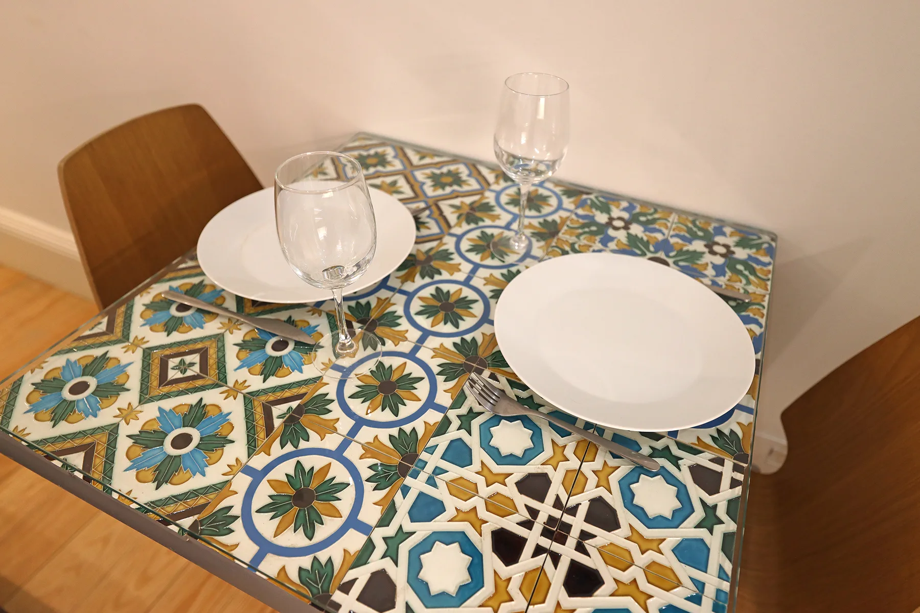 A small dining table with colorful patterned tiles is set with plates and glasses.