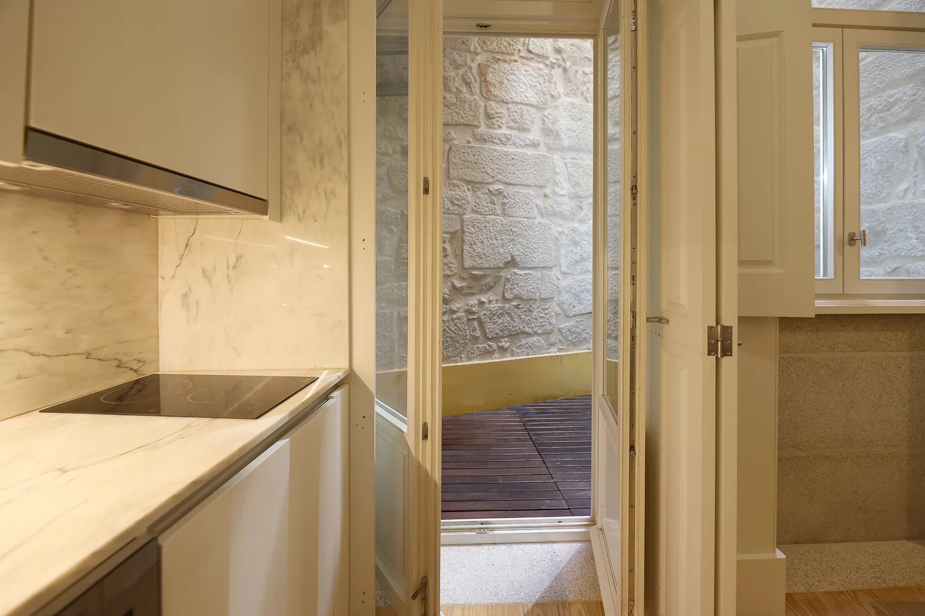 A kitchen opens onto a small terrace with a stone wall and wooden decking.