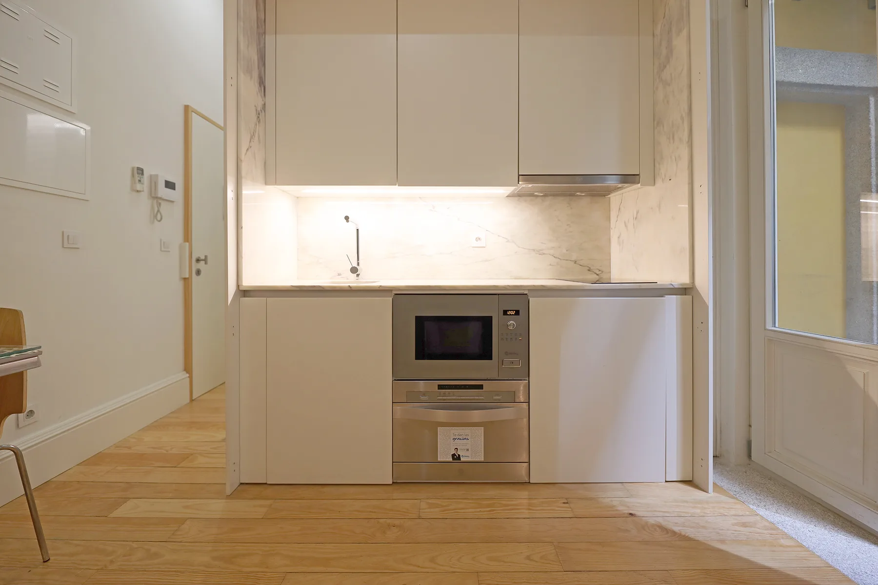 A compact kitchen with built-in appliances and light wood flooring.