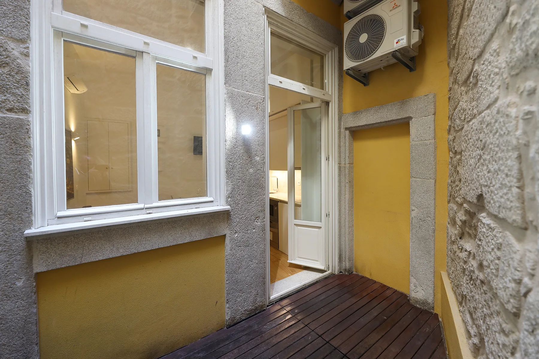 A narrow terrace with a wood-plank floor beside a studio entrance.