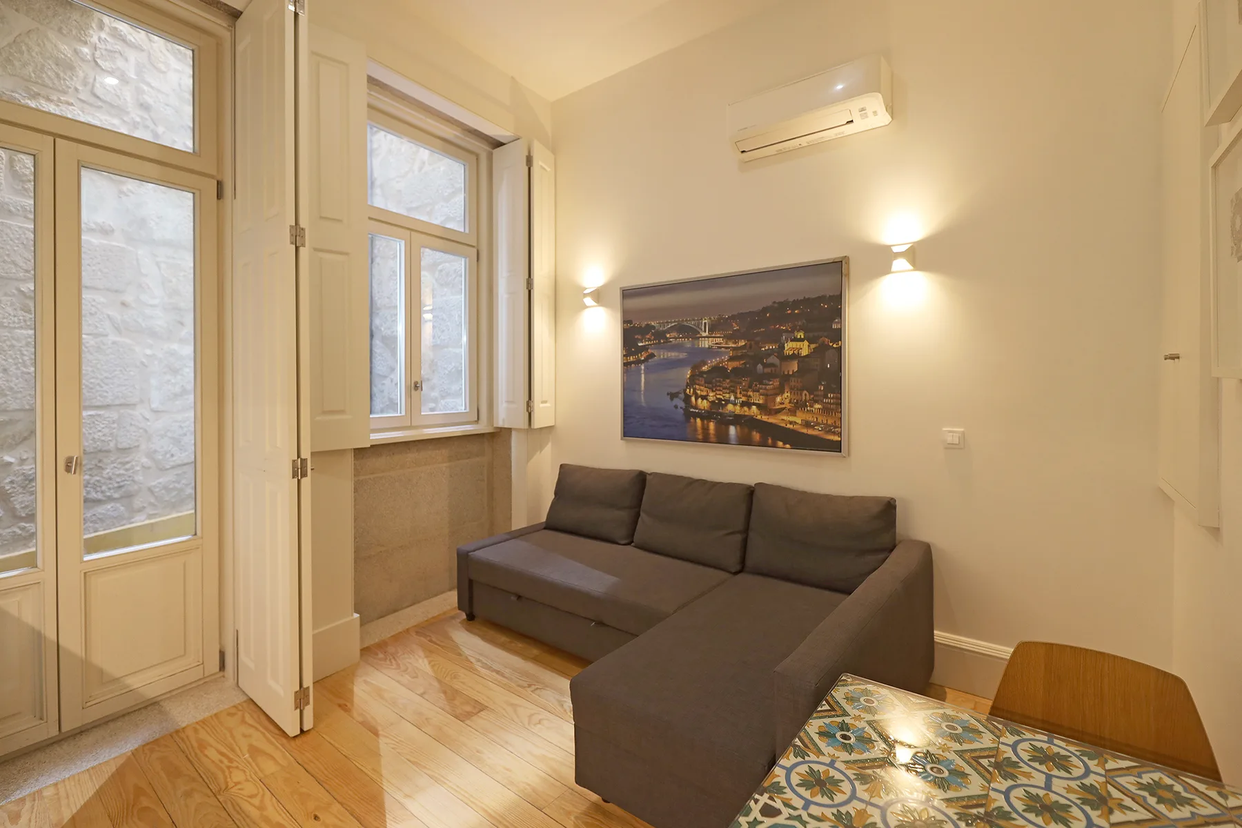 A living area with a sectional sofa, tall windows, and a tiled table.