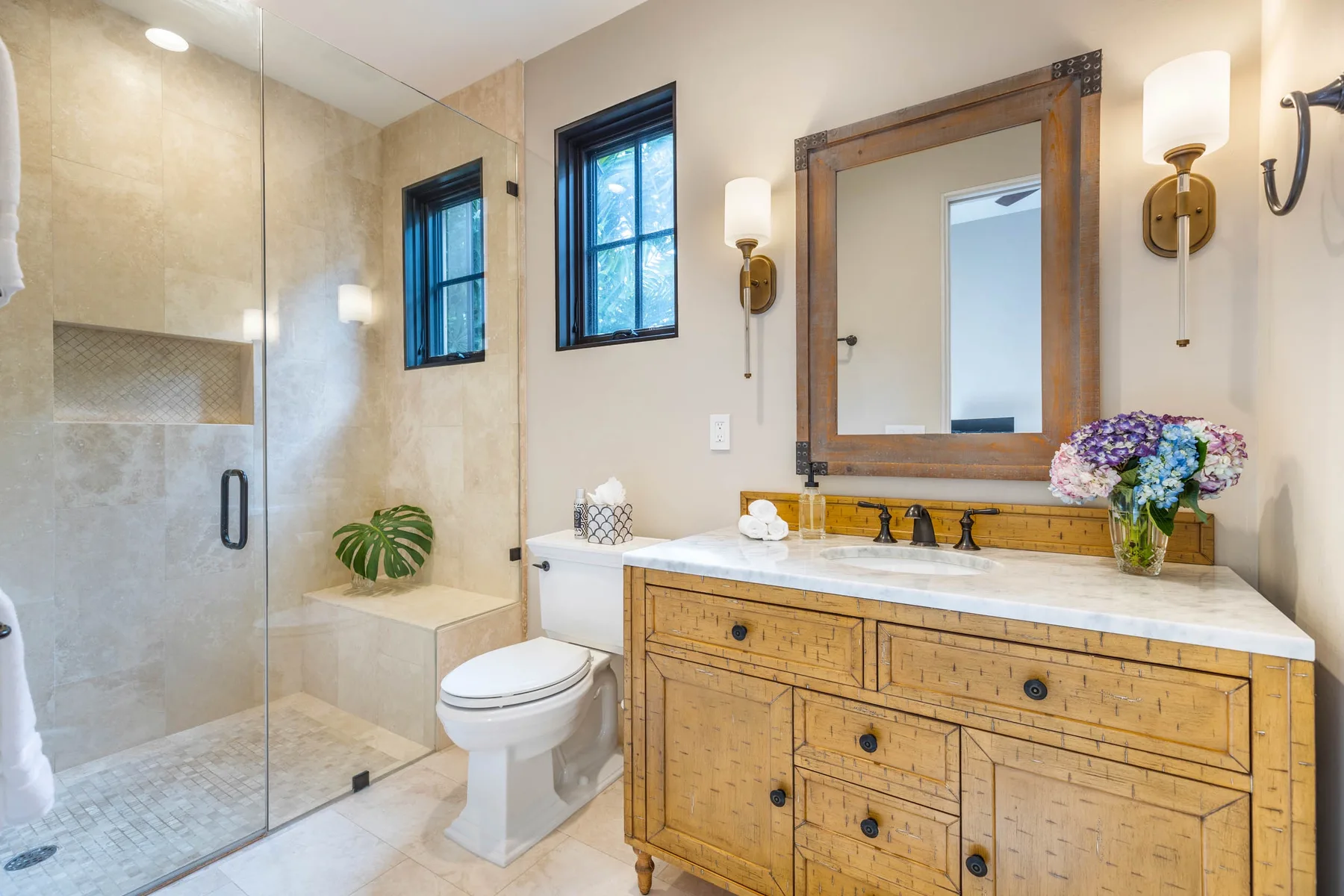 A bright bathroom with a glass shower, vanity, and large mirror.