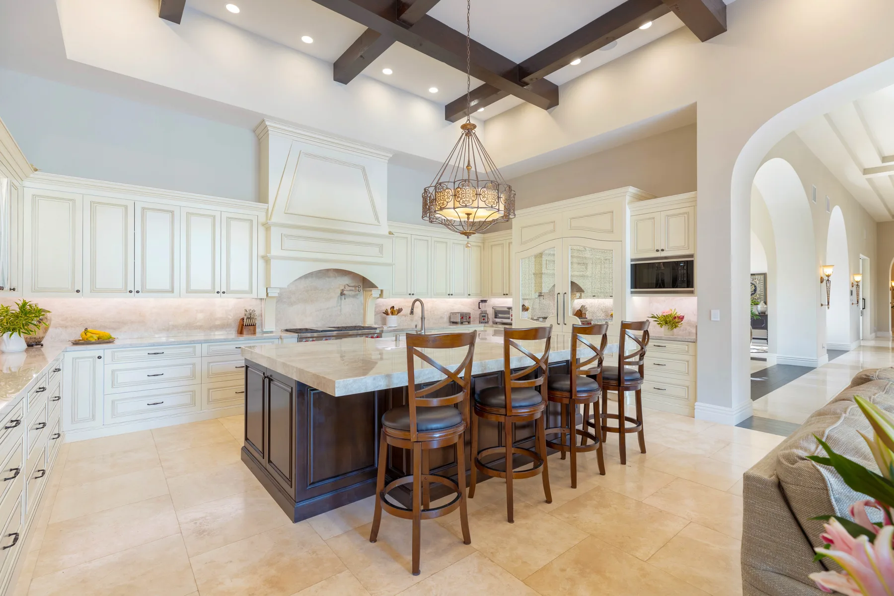 A spacious kitchen features white cabinetry, a central island, and dark ceiling beams.