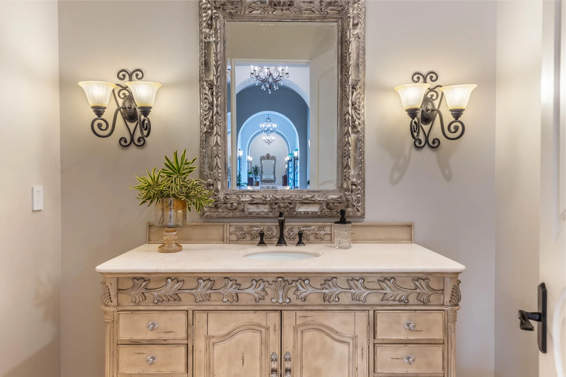 A bathroom vanity with a large framed mirror and wall sconces.