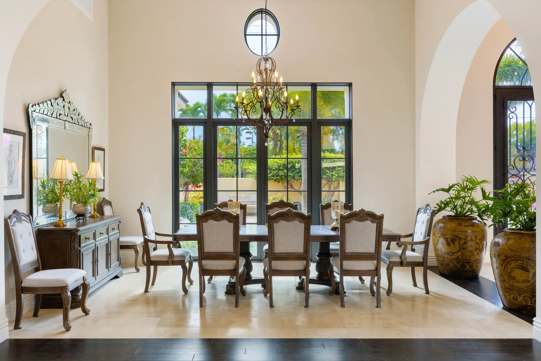 A formal dining room has a long table surrounded by chairs beneath a chandelier.