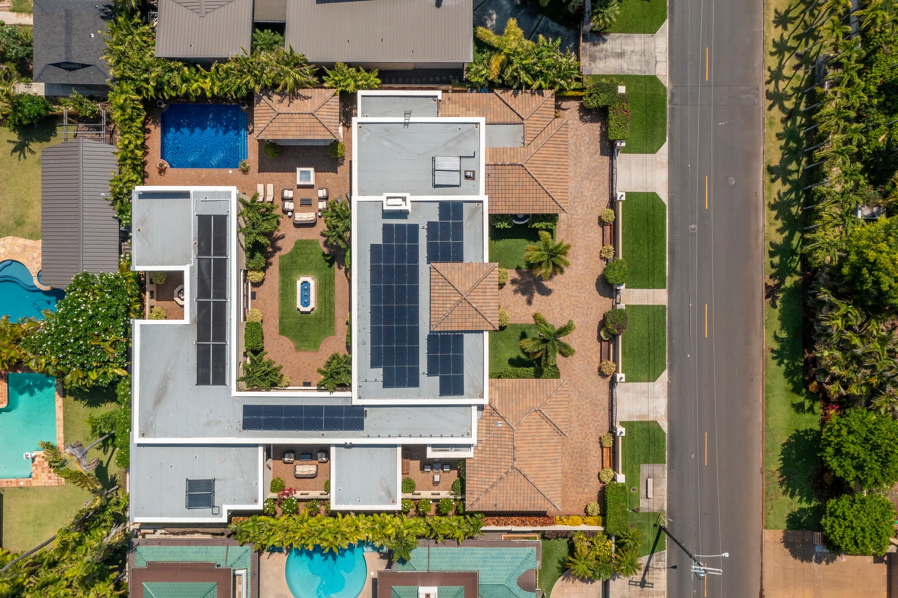 Aerial view of a large house with rooftop solar panels and a surrounding paved yard.