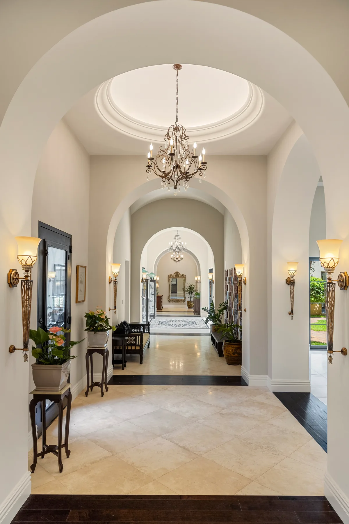 A bright arched entry hall with a chandelier and decorative plants.