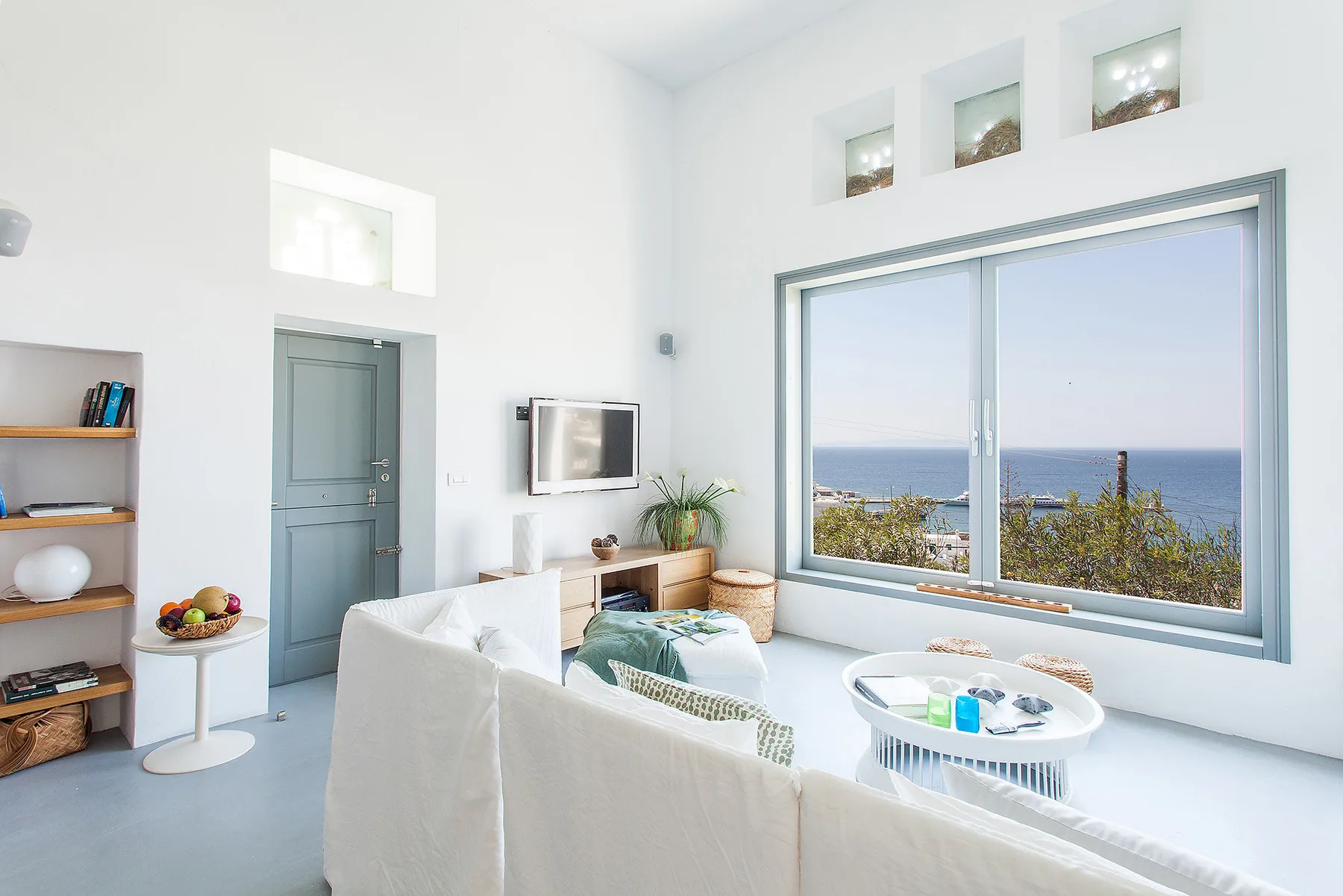 A bright living room with seating and a large window overlooking the sea.