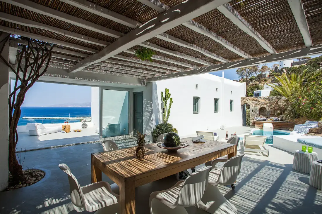 Una zona de comedor exterior a la sombra da a una piscina y al mar.