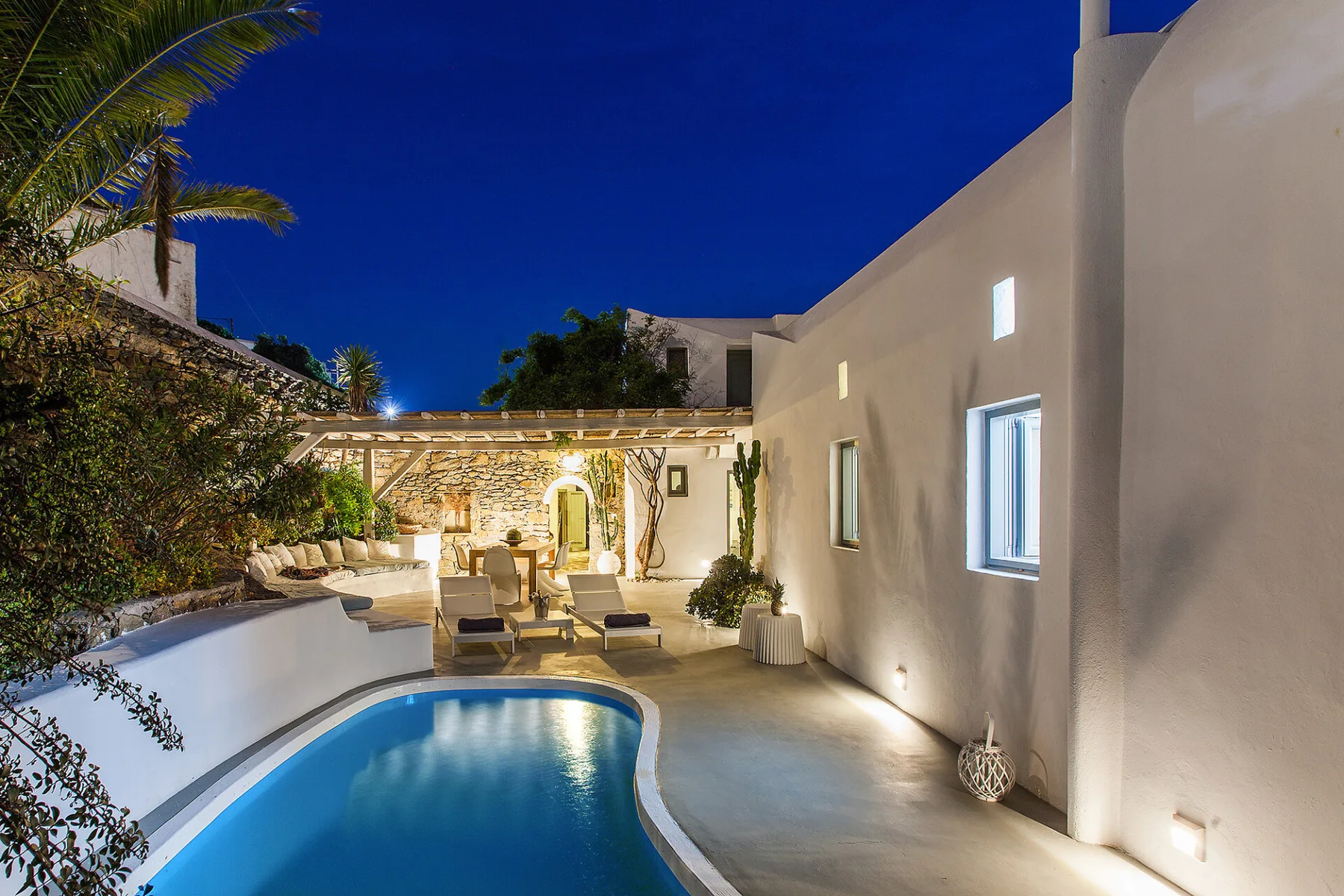 Una piscina en un patio junto a un edificio blanco y asientos al aire libre por la noche.