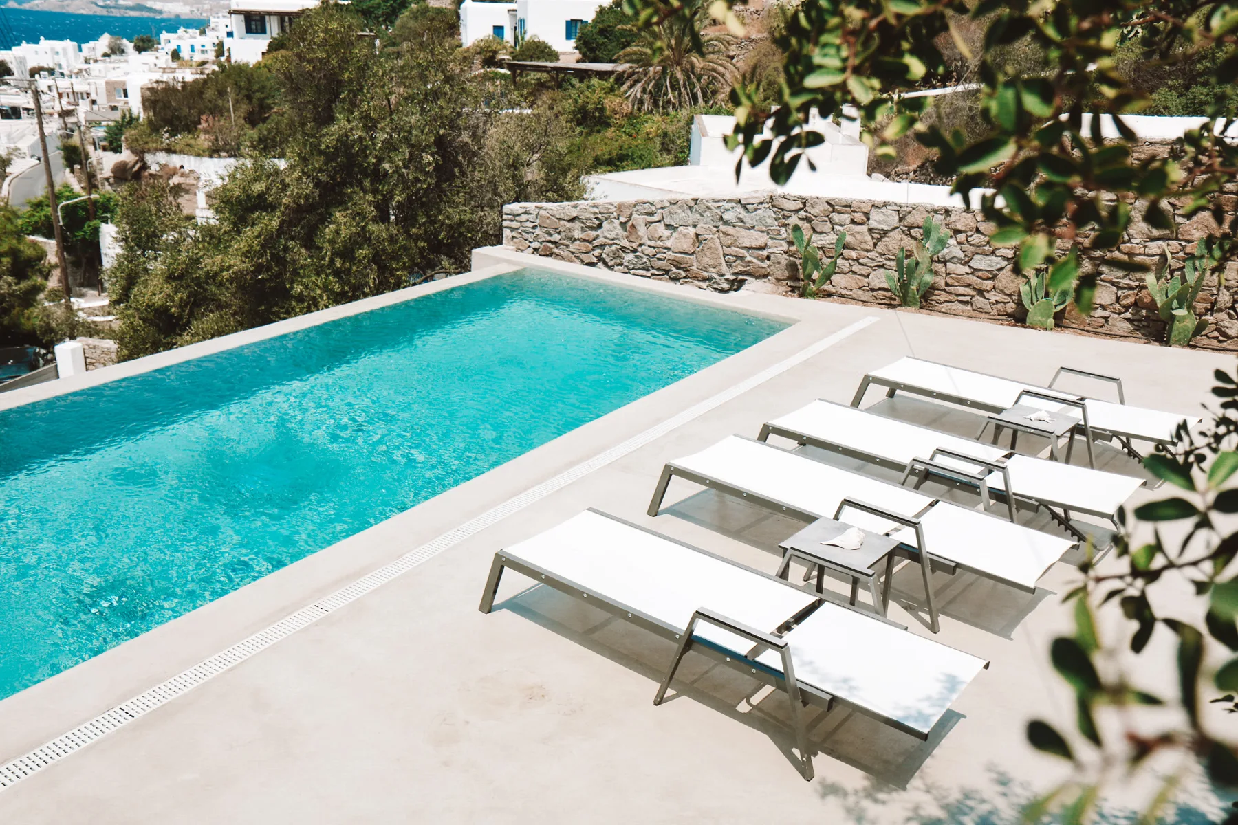Una piscina al aire libre junto a una terraza soleada con asientos.