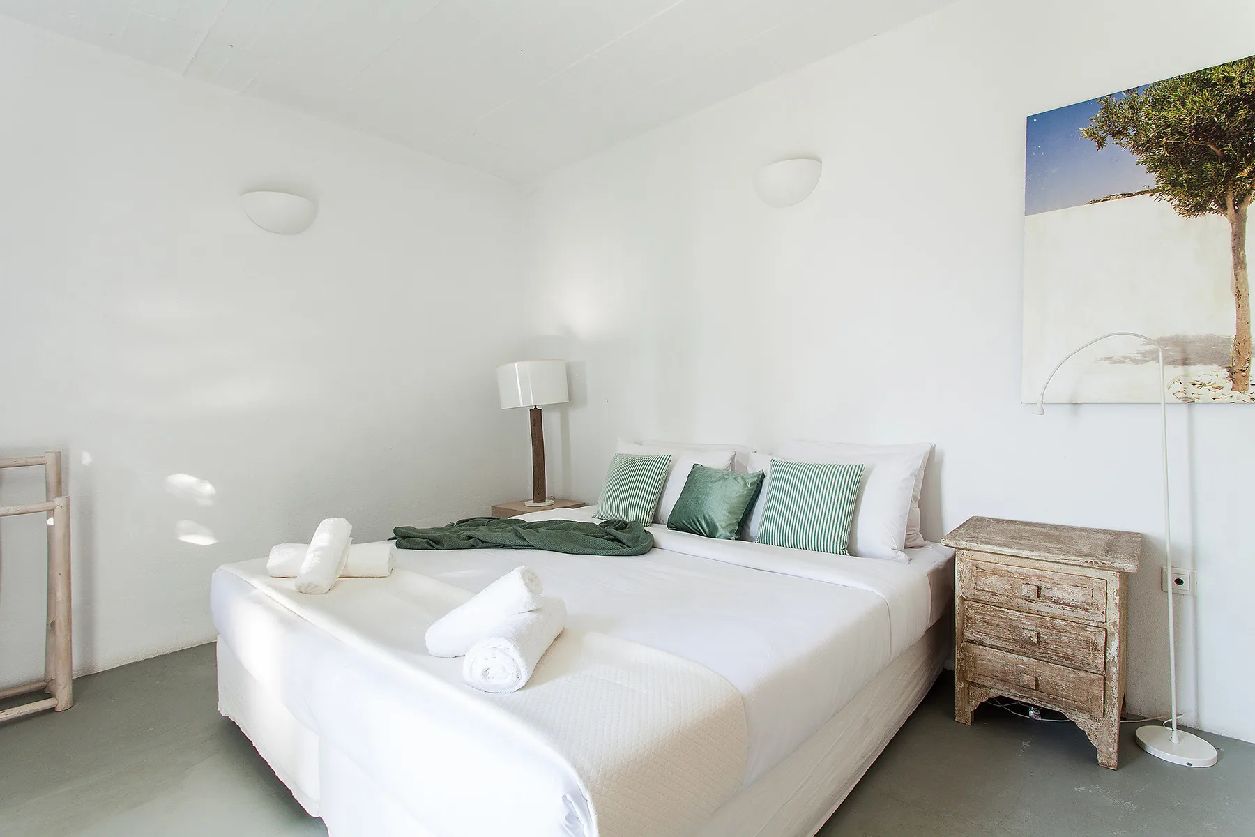 Un dormitorio luminoso con una cama blanca y cojines verdes.