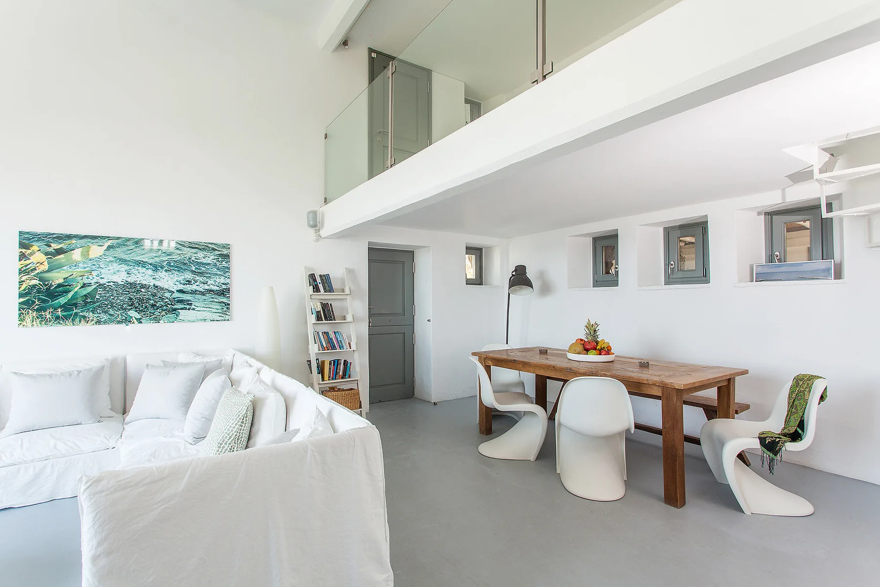 A bright living and dining area with white seating and a wooden table.