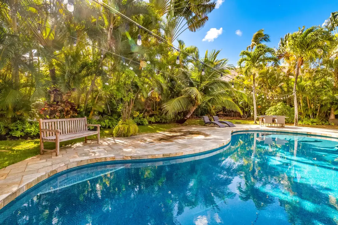 Una piscina al aire libre bordea un patio pavimentado y vegetación tropical.