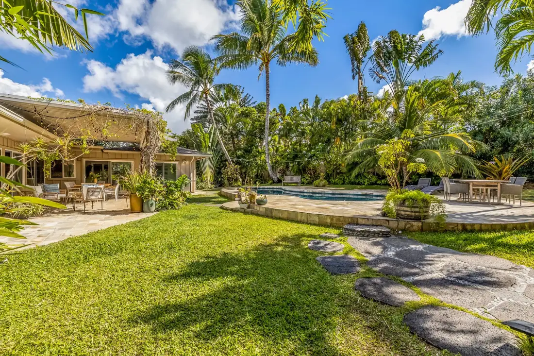 Una zona de piscina tropical al aire libre con césped y palmeras alrededor.