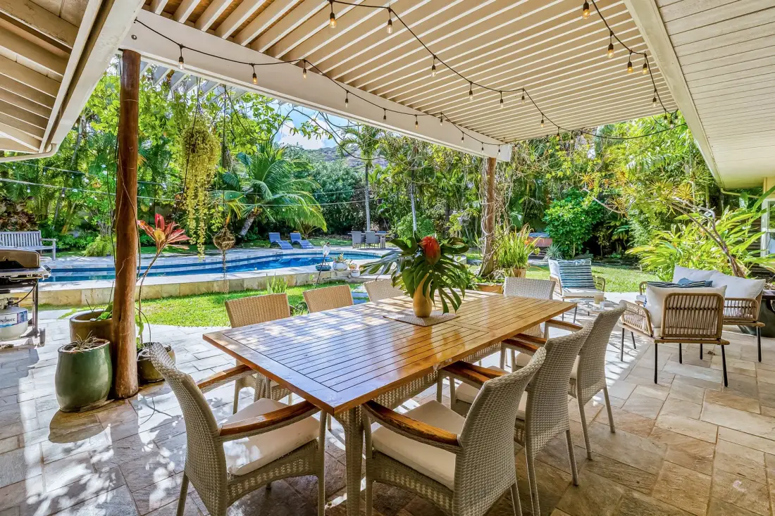 Un patio cubierto tiene una mesa de comedor y asientos junto a una piscina.