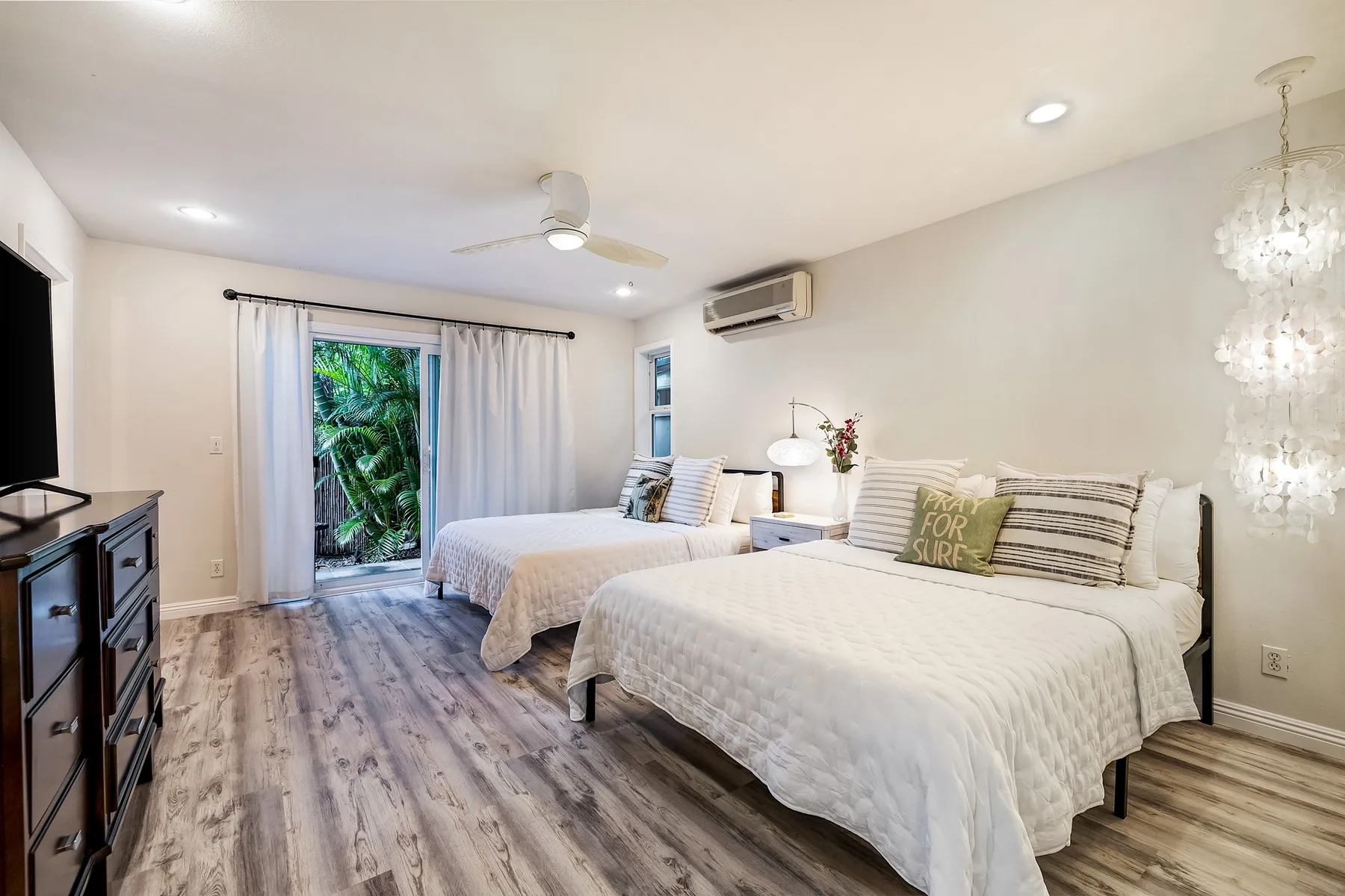 Un dormitorio luminoso con dos camas, ropa de cama blanca y una ventana con vista a la vegetación.