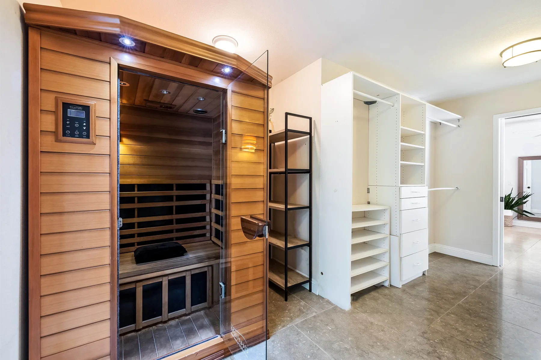 Una sauna junto a estantes abiertos y armarios en una habitación luminosa con suelo de baldosas.