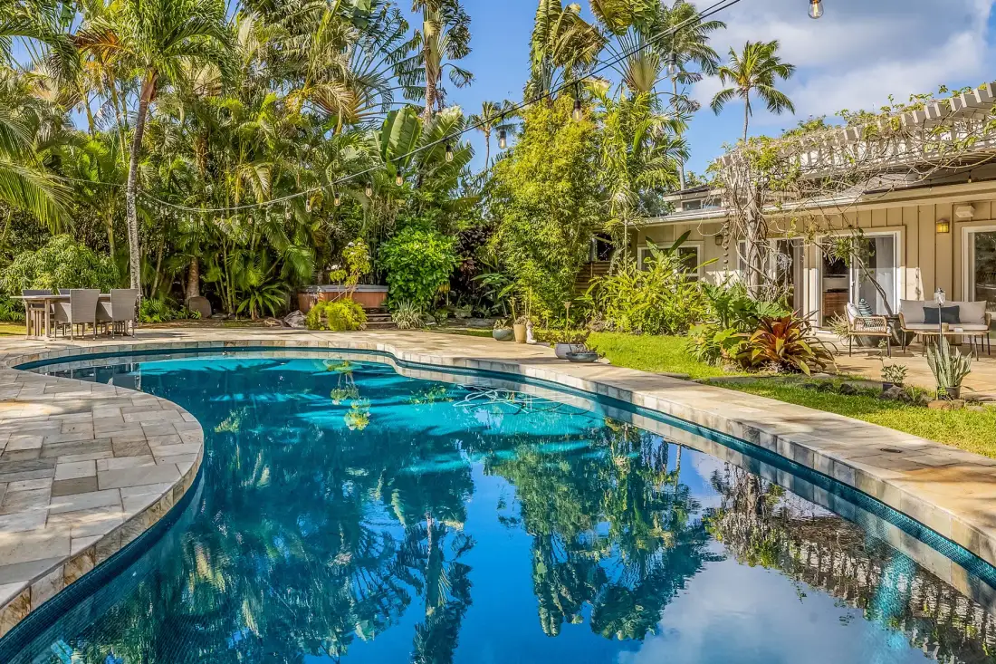 Una piscina curva está junto a un patio rodeado de abundante vegetación tropical.