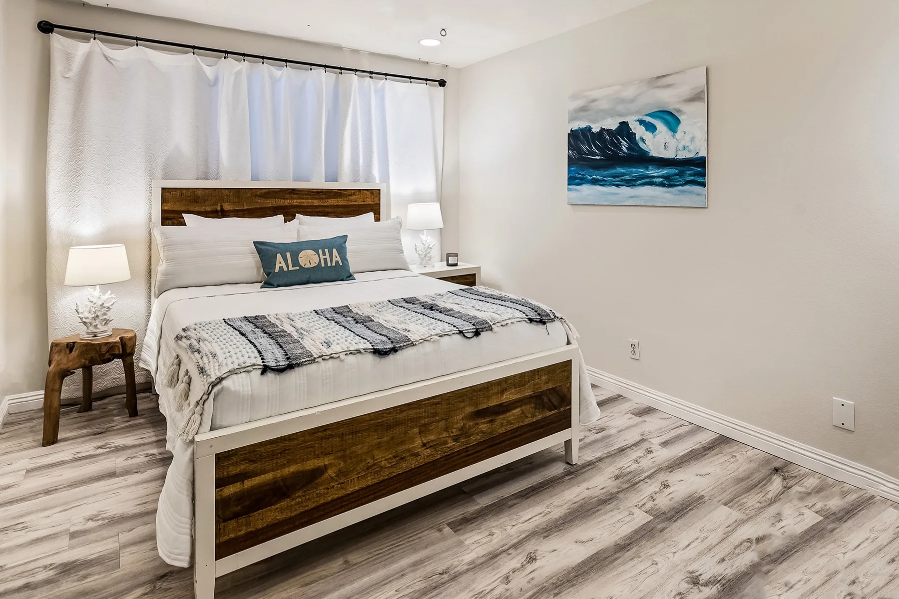 Un dormitorio con una cama de madera, cortinas blancas y un cuadro del océano en la pared.