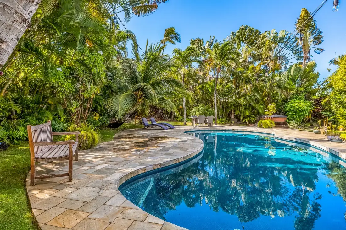 Una piscina está rodeada por una terraza pavimentada y exuberante vegetación tropical.
