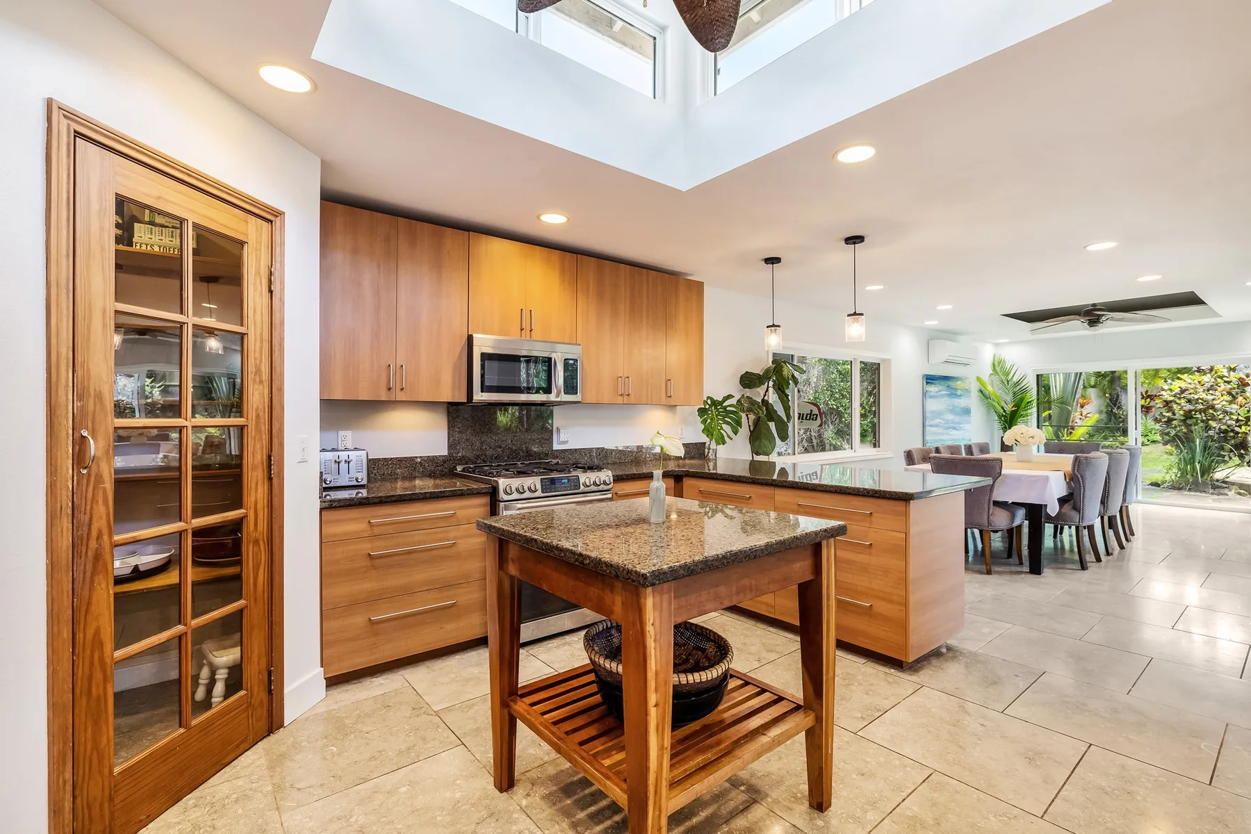 Una cocina luminosa con gabinetes de madera e isla central se abre a un comedor.