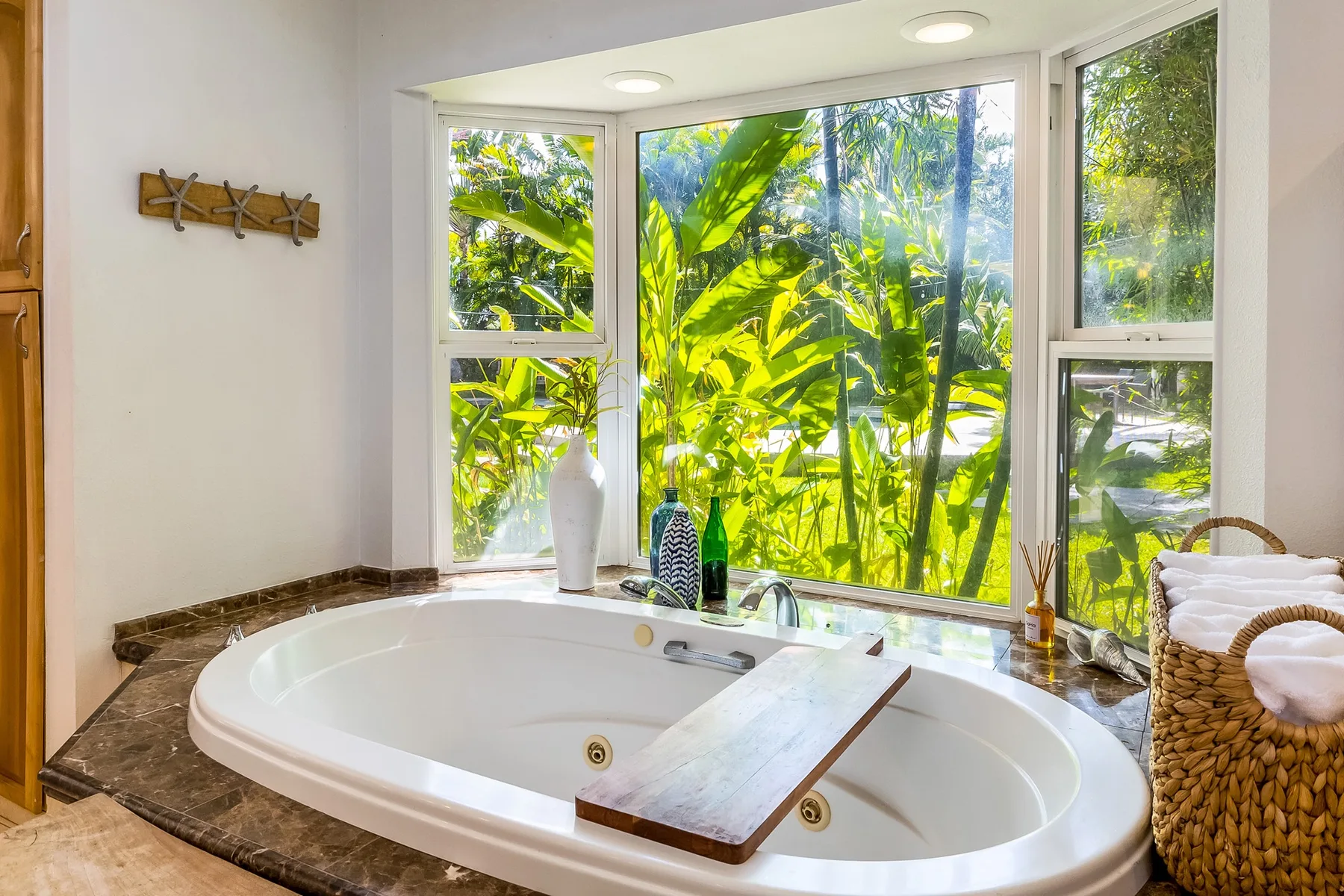 Un baño con una gran bañera blanca junto a ventanas con vista a una vegetación frondosa.