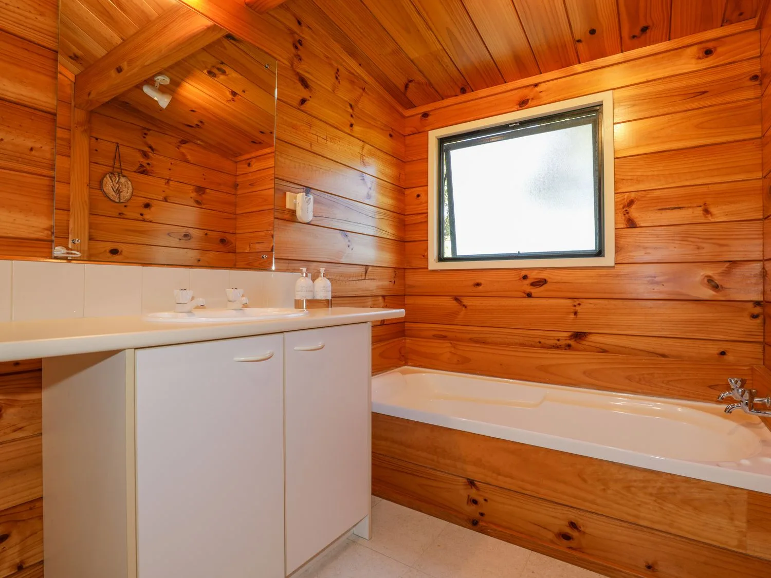 Un baño con un mueble blanco con lavabo, bañera y ventana.