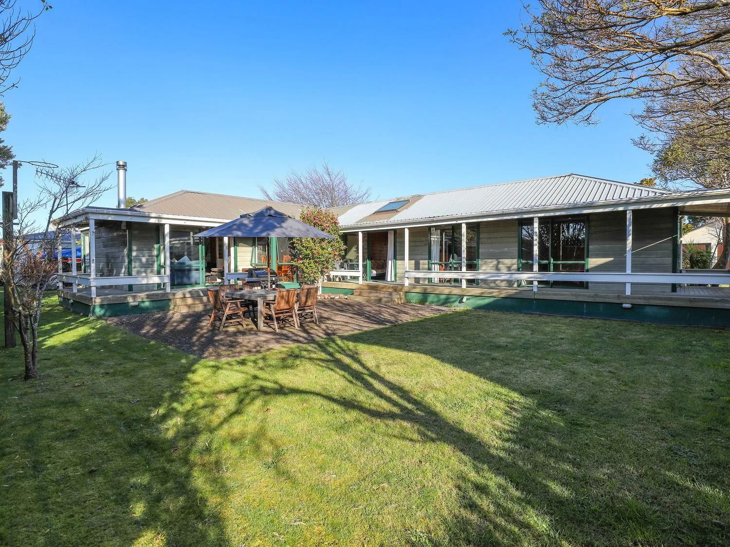 A house with a metal roof a wooden patio set with an umbrella and green grass in the yard at Five Mile Yay - Five Mile Bay Holiday Home in Waitahanui 12km from Taupo