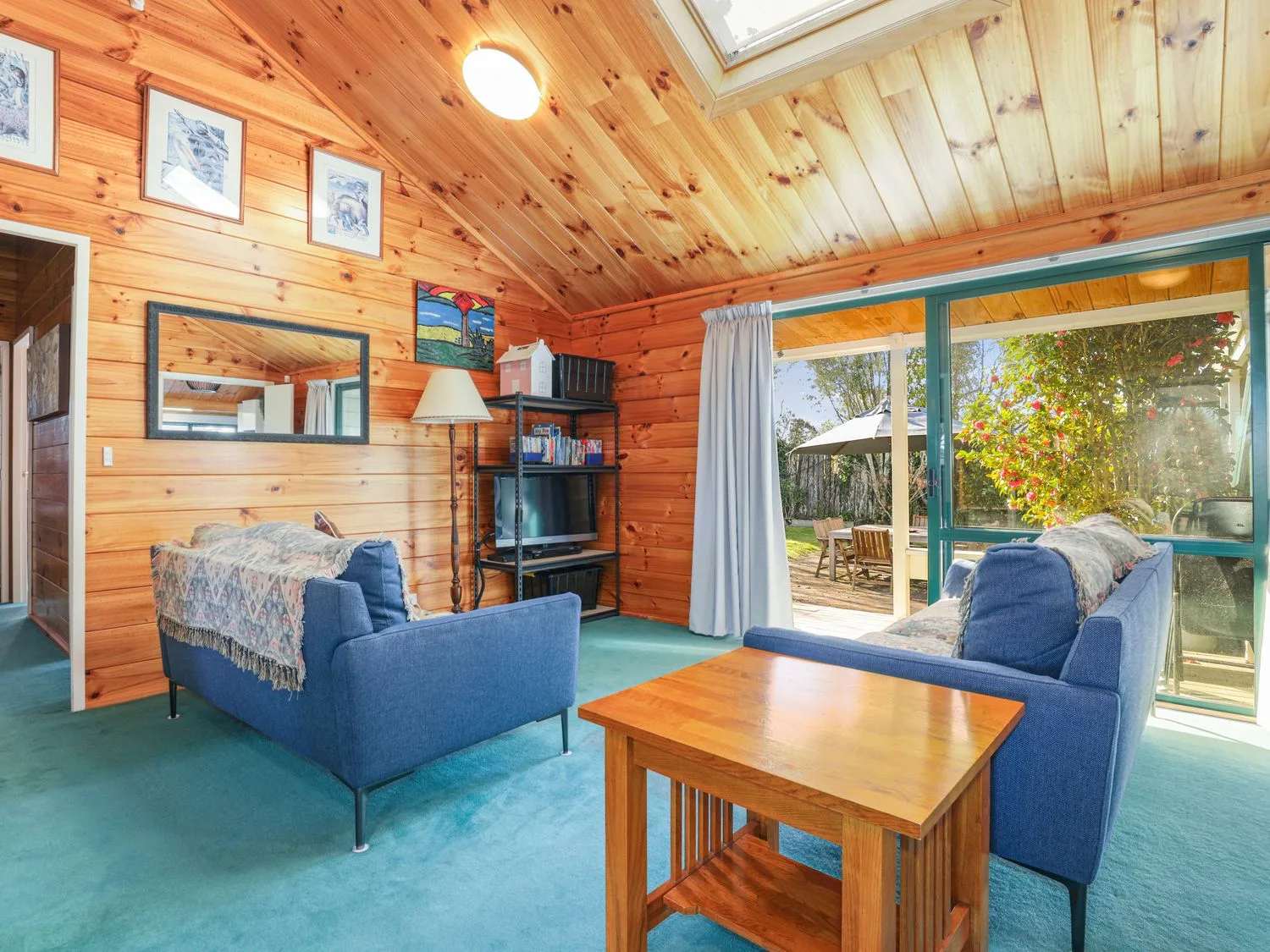 Una sala de estar con asientos azules, una mesa de centro de madera y grandes ventanas con vistas al jardín.