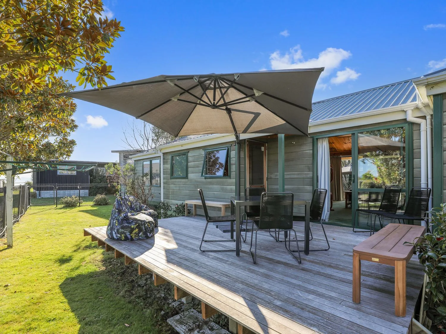 A wooden deck with an umbrella, outdoor seating, and a table beside a house.