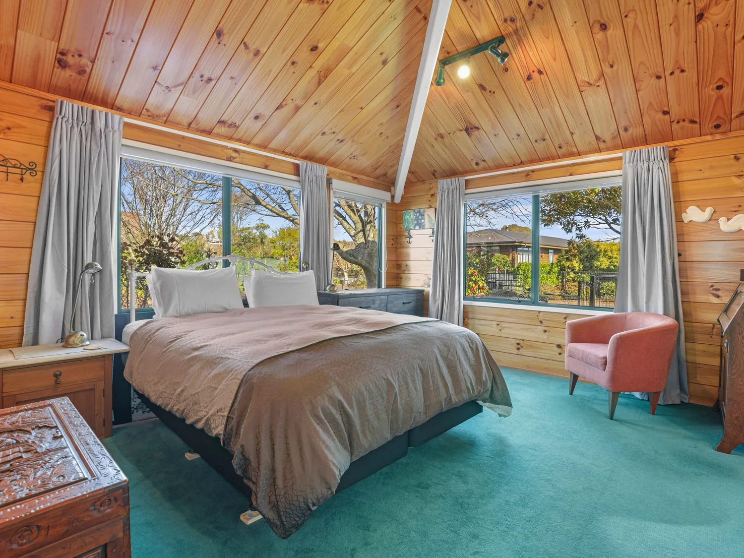 Un dormitorio con una cama grande, ventanas y paredes y techo revestidos de madera.