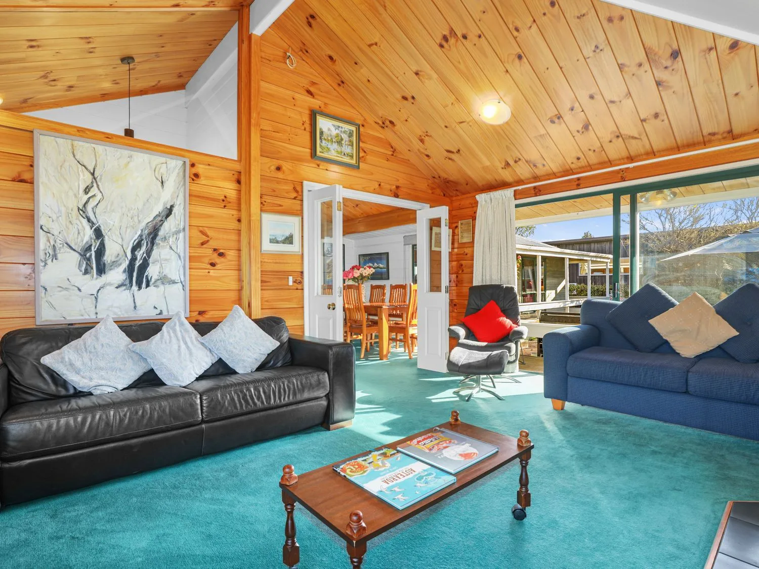 A wood-paneled living room with seating and a coffee table, opening onto a dining area.