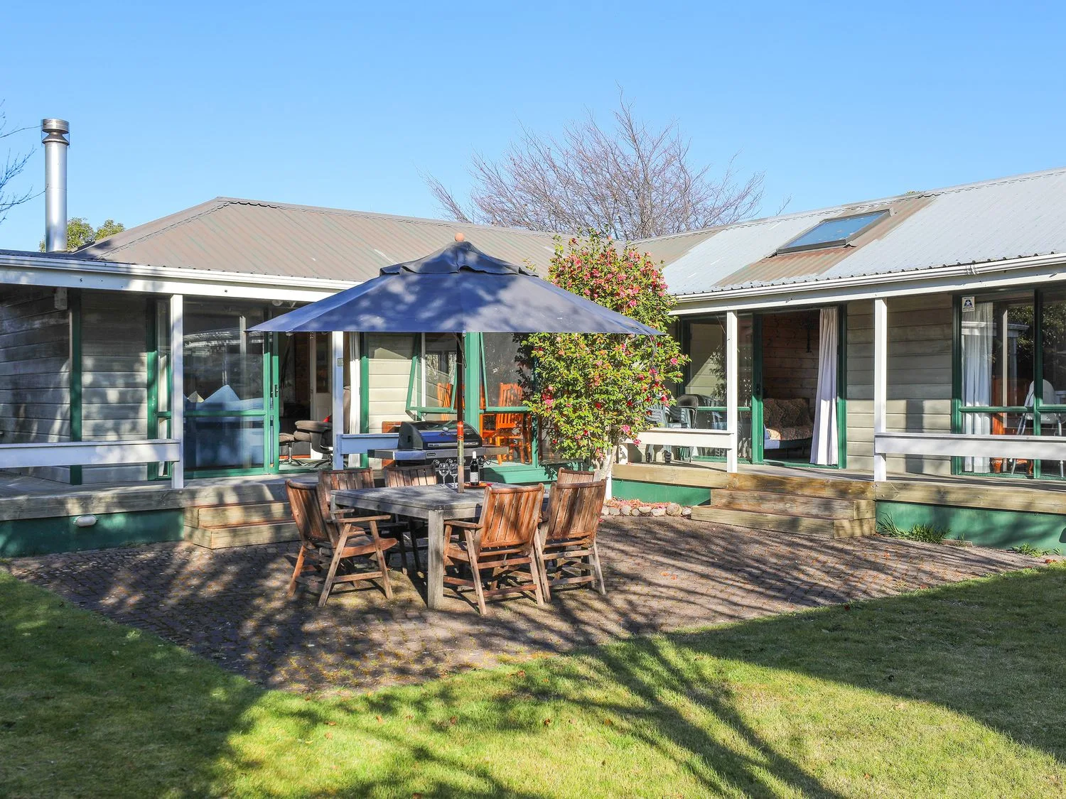 An outdoor patio with a wooden table and chairs beneath a blue umbrella.