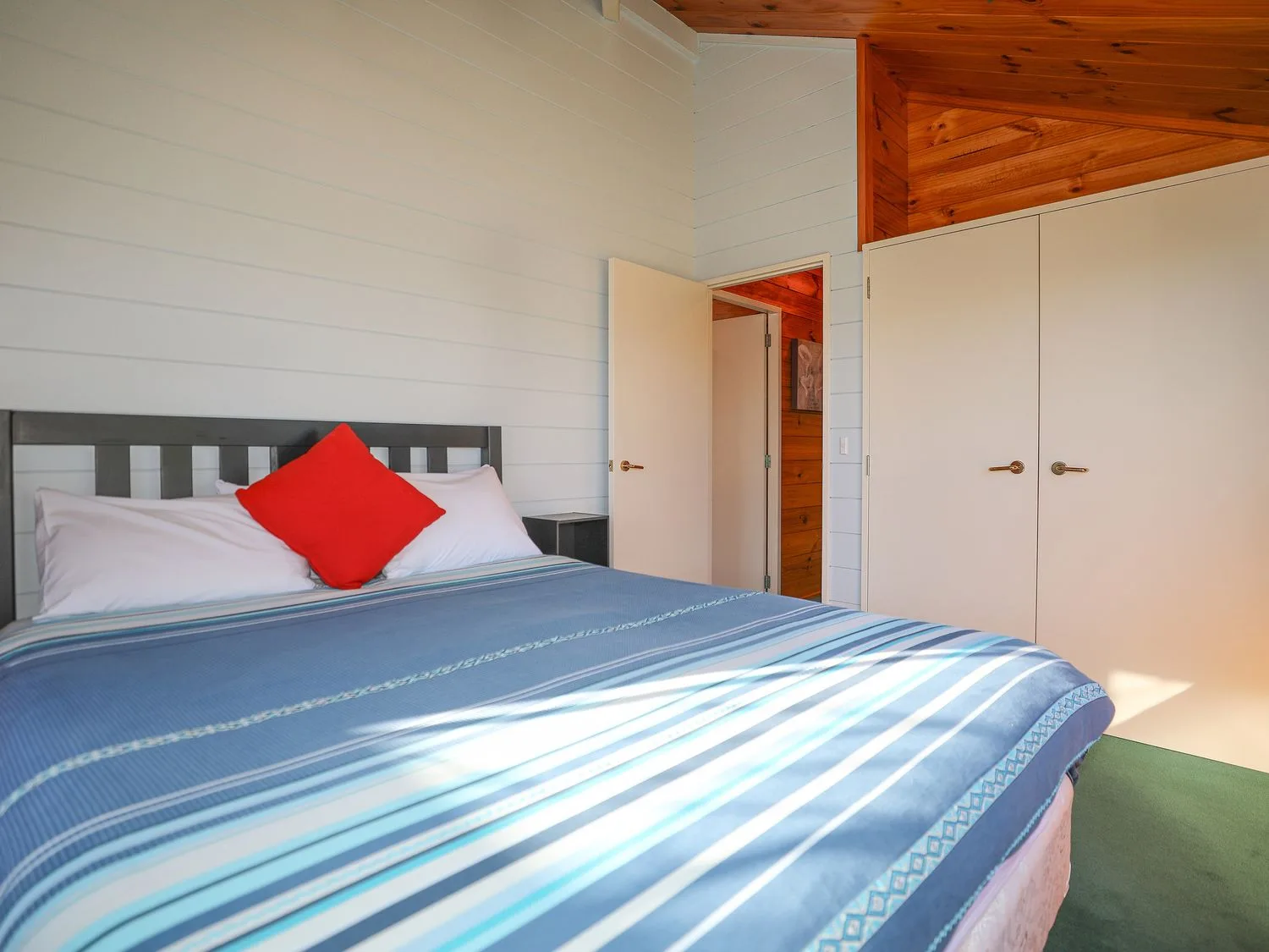 Un dormitorio con una cama cubierta con una manta de rayas azules y una almohada roja.