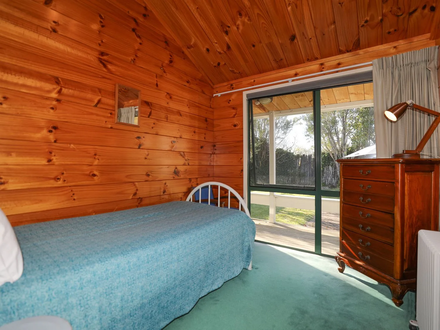Un dormitorio con una cama junto a una cómoda de madera y puertas corredizas de vidrio.
