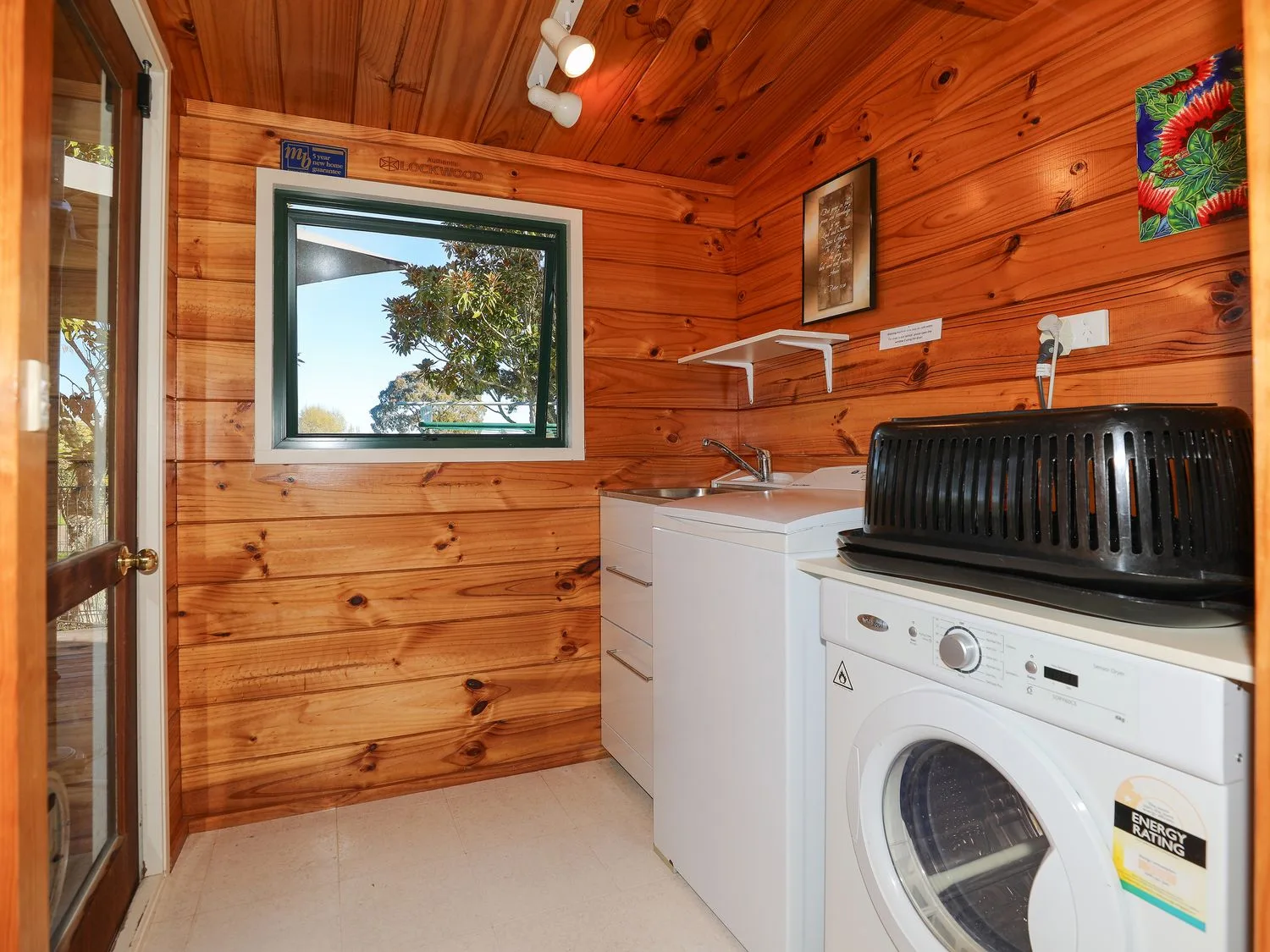 Un cuarto de lavado con paredes revestidas de madera, una lavadora, un lavadero y una ventana pequeña en Five Mile Yay - Five Mile Bay Holiday Home, en Waitahanui, a 12 km de Taupo.