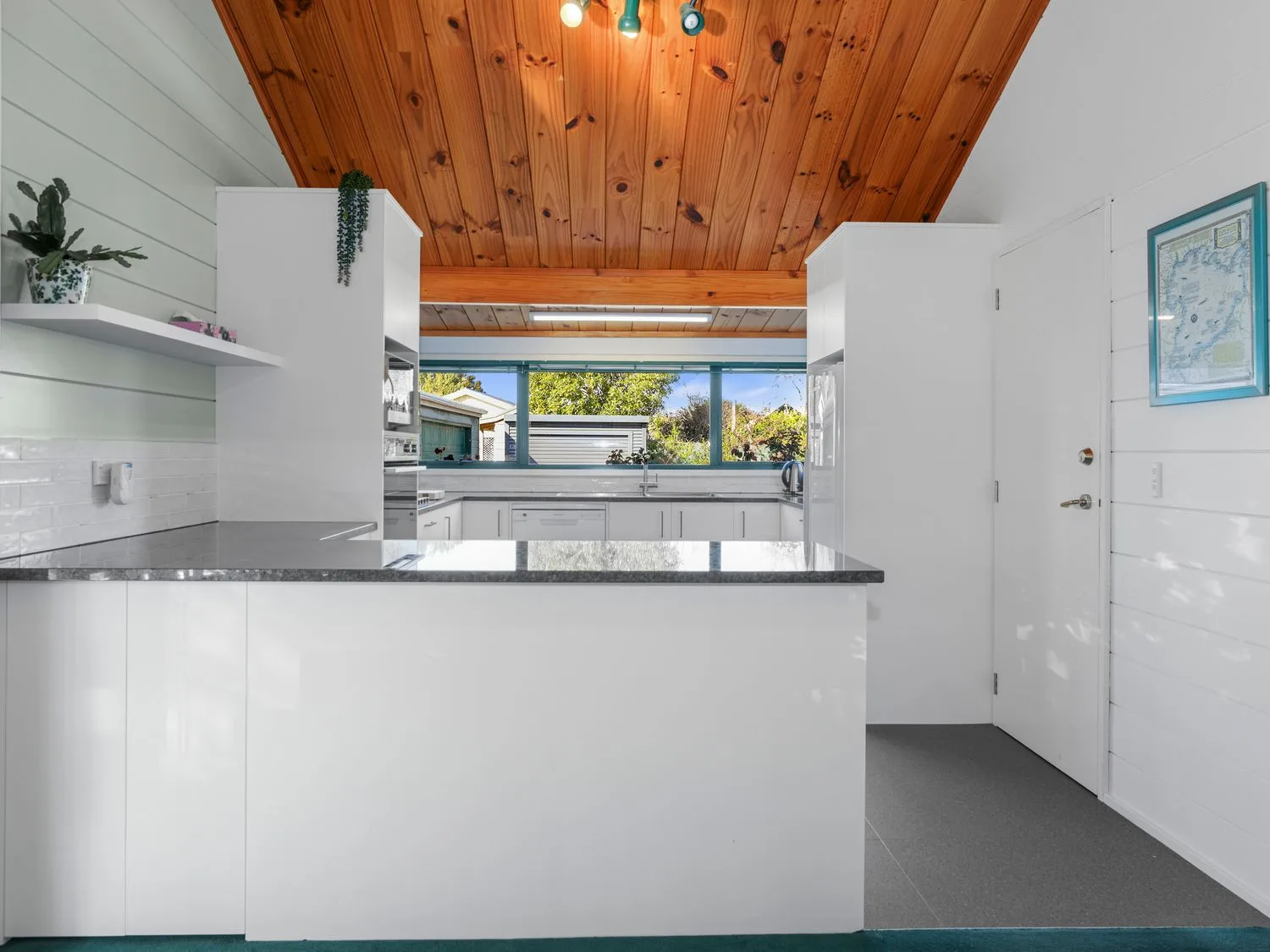 Una cocina con muebles blancos, encimeras grises y techo de madera.