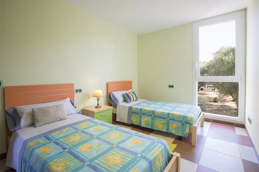 A bright bedroom with two beds covered in colorful patterned bedding.