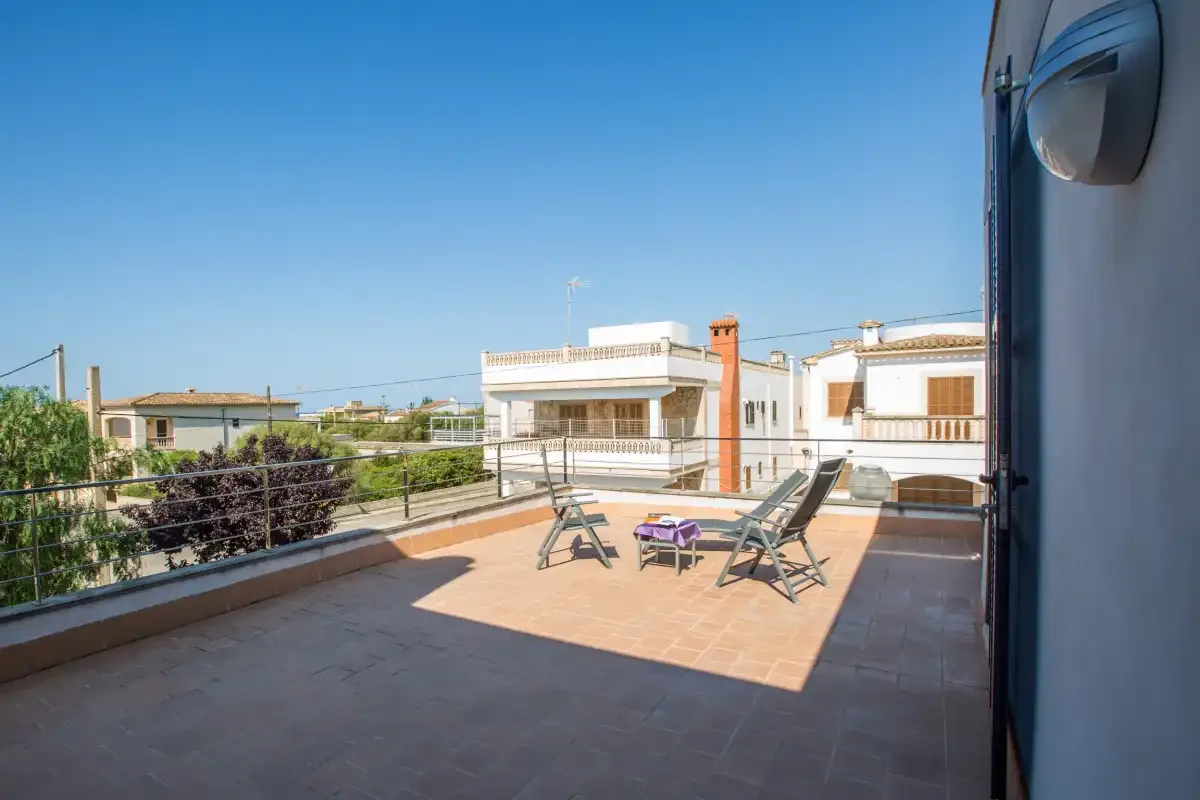 A sunny rooftop terrace with outdoor seating and views of nearby homes.