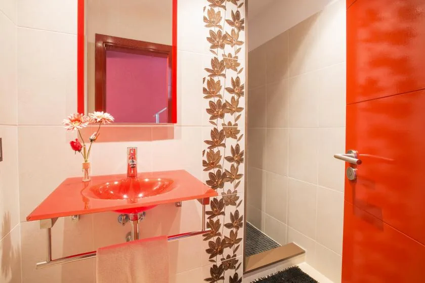A tiled bathroom with a red vanity, mirror, and shower area.